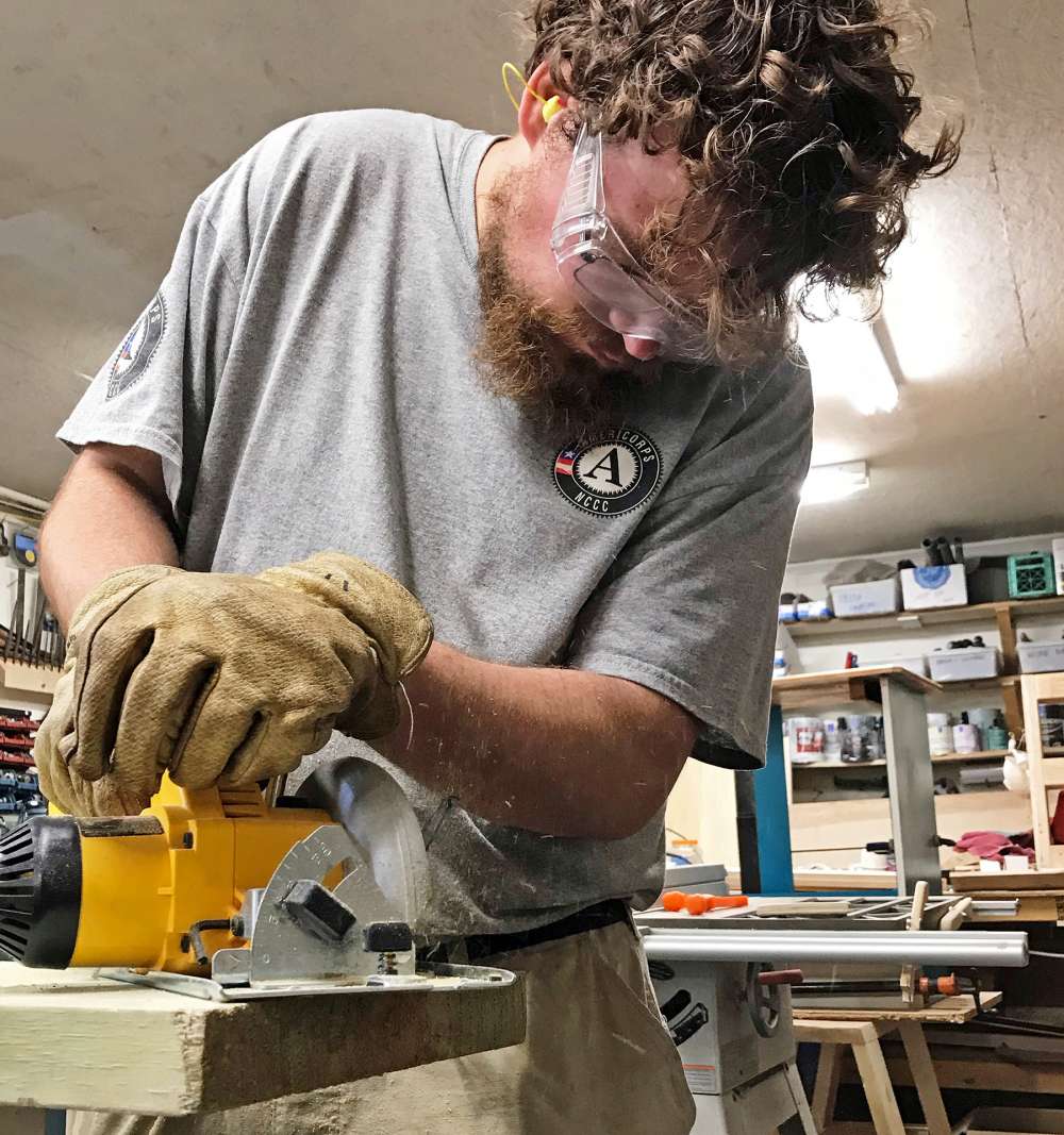 AmeriCorps volunteer cutting a board.