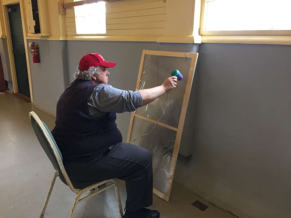 WindowDressers volunteer heats plastic to make it taut on the frame.