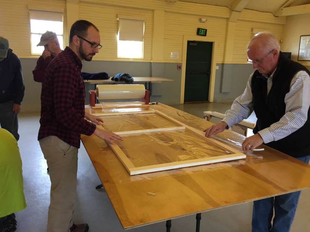 WindowDressers volunteers stretch plastic over a wooden frame.