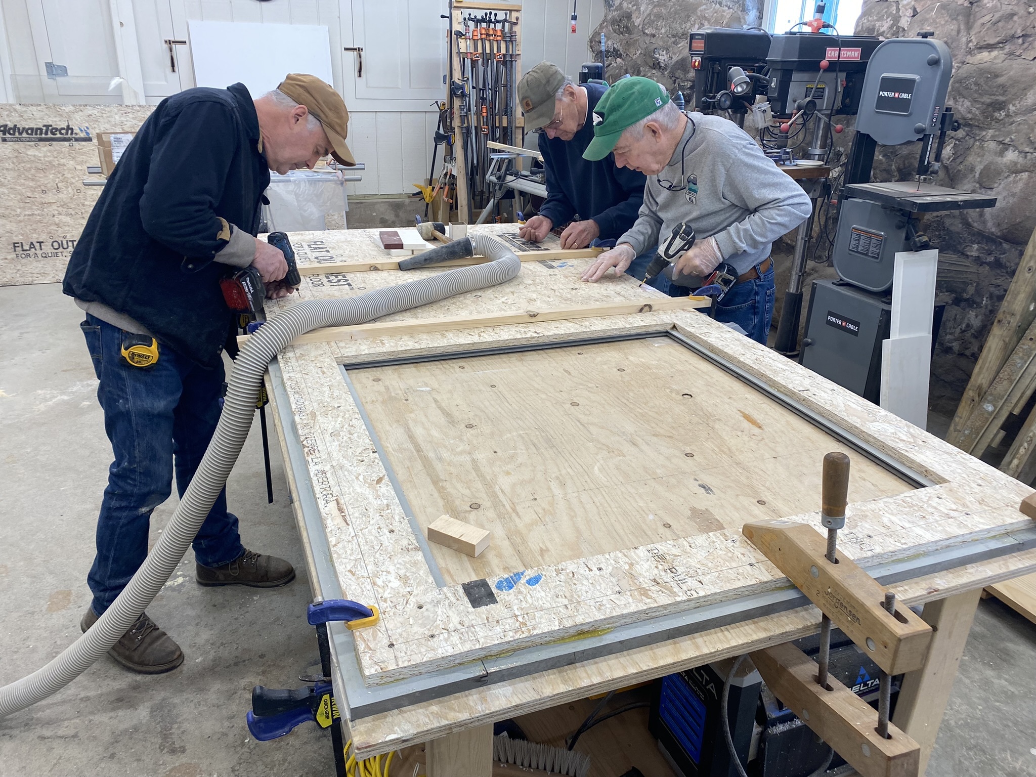 Frank Heller and Dave Harrison measure and mark a door under construction as Brian Greenwood prepares to drill.