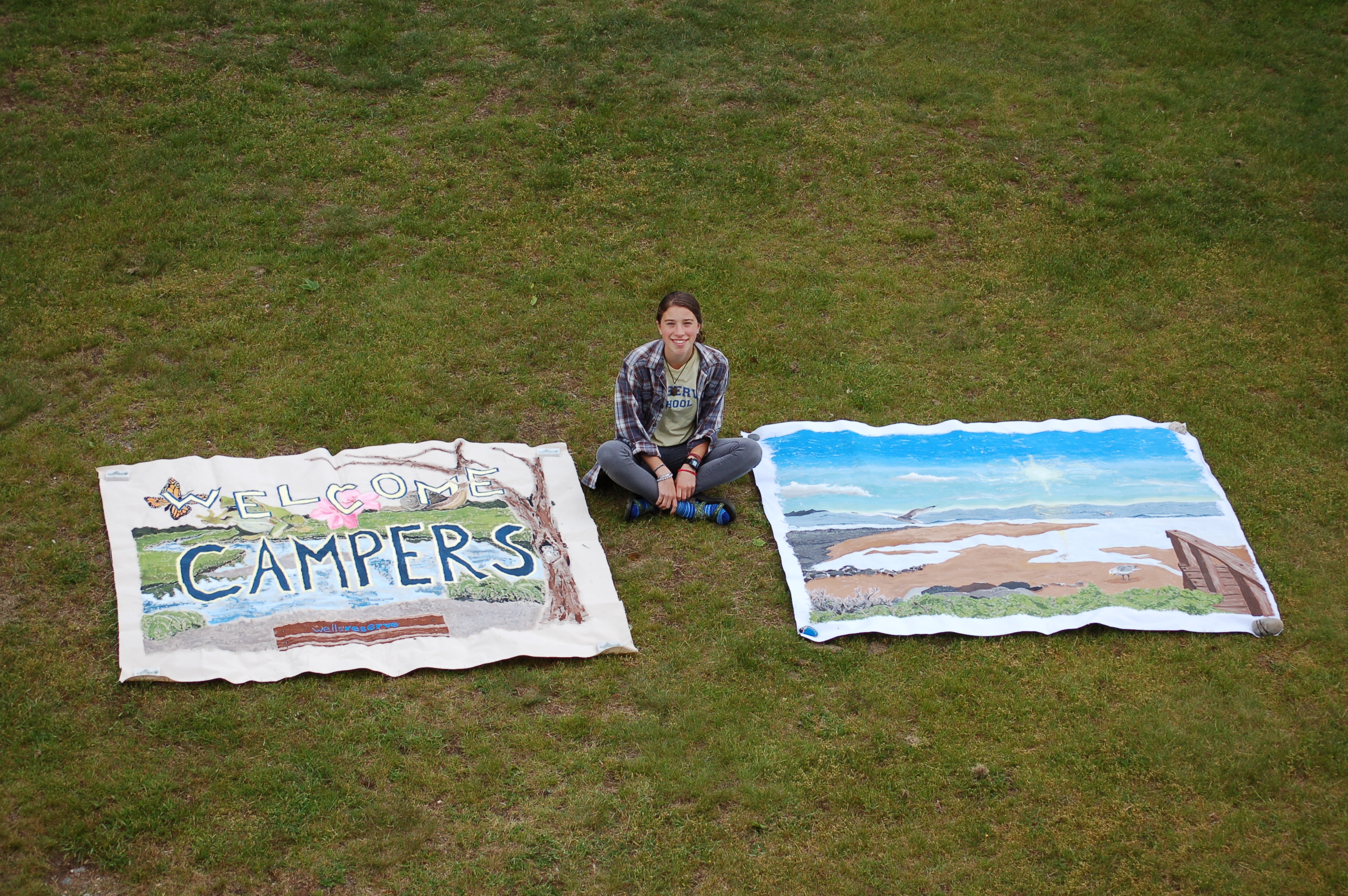Emma Shedd sits with the two murals she painted for use in our education programs.